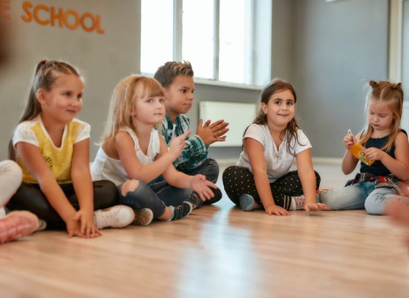 Taking a break. A group of little cute girls and boys sitting on the floor and talking to each other in the dance studio. Choreography class