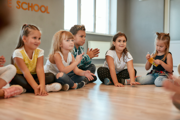 Taking a break. A group of little cute girls and boys sitting on the floor and talking to each other in the dance studio. Choreography class