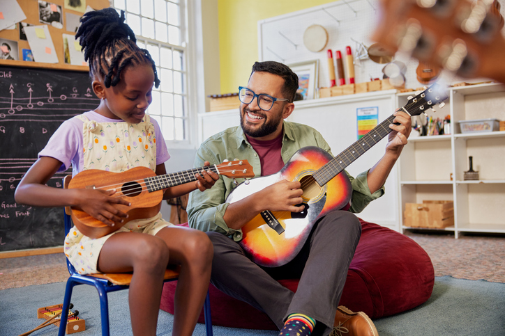 Teacher and students playing guitar together during music lesson